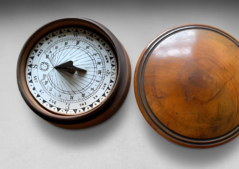 A circular turned wood case with a domed lid and concentric outer rings in a warm brown polished finish. View III
