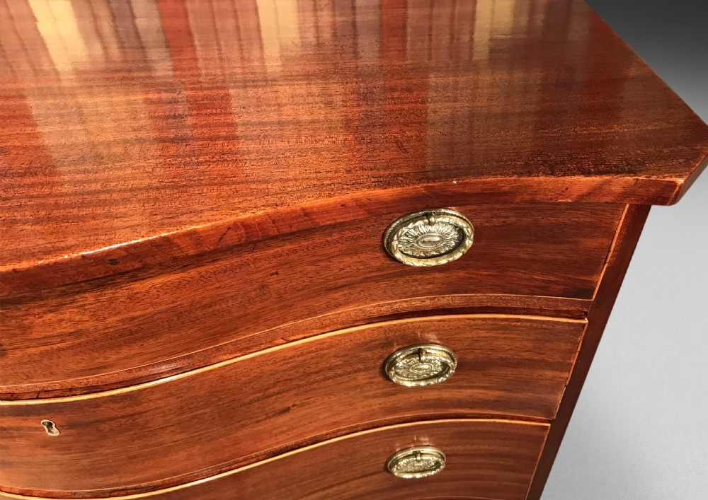 A George III mahogany chest of drawers featuring a serpentine front, four graduated drawers with brass oval handles, and bracket feet. View VII
