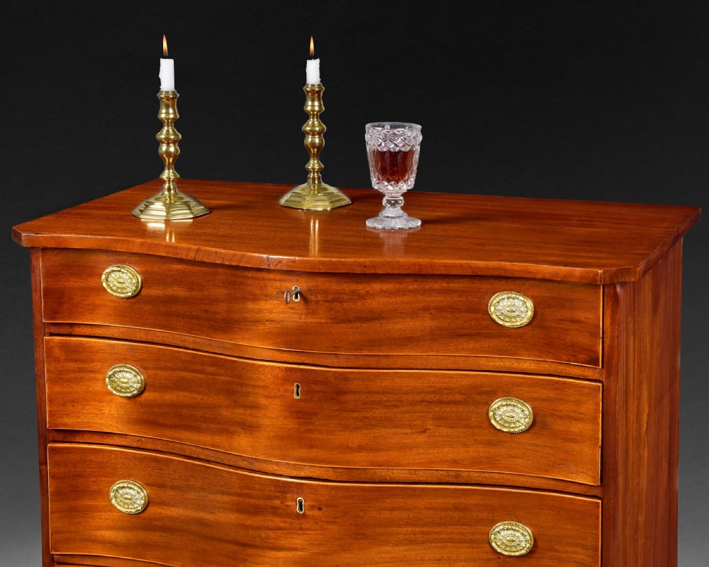 A George III mahogany chest of drawers featuring a serpentine front, four graduated drawers with brass oval handles, and bracket feet. View VIII