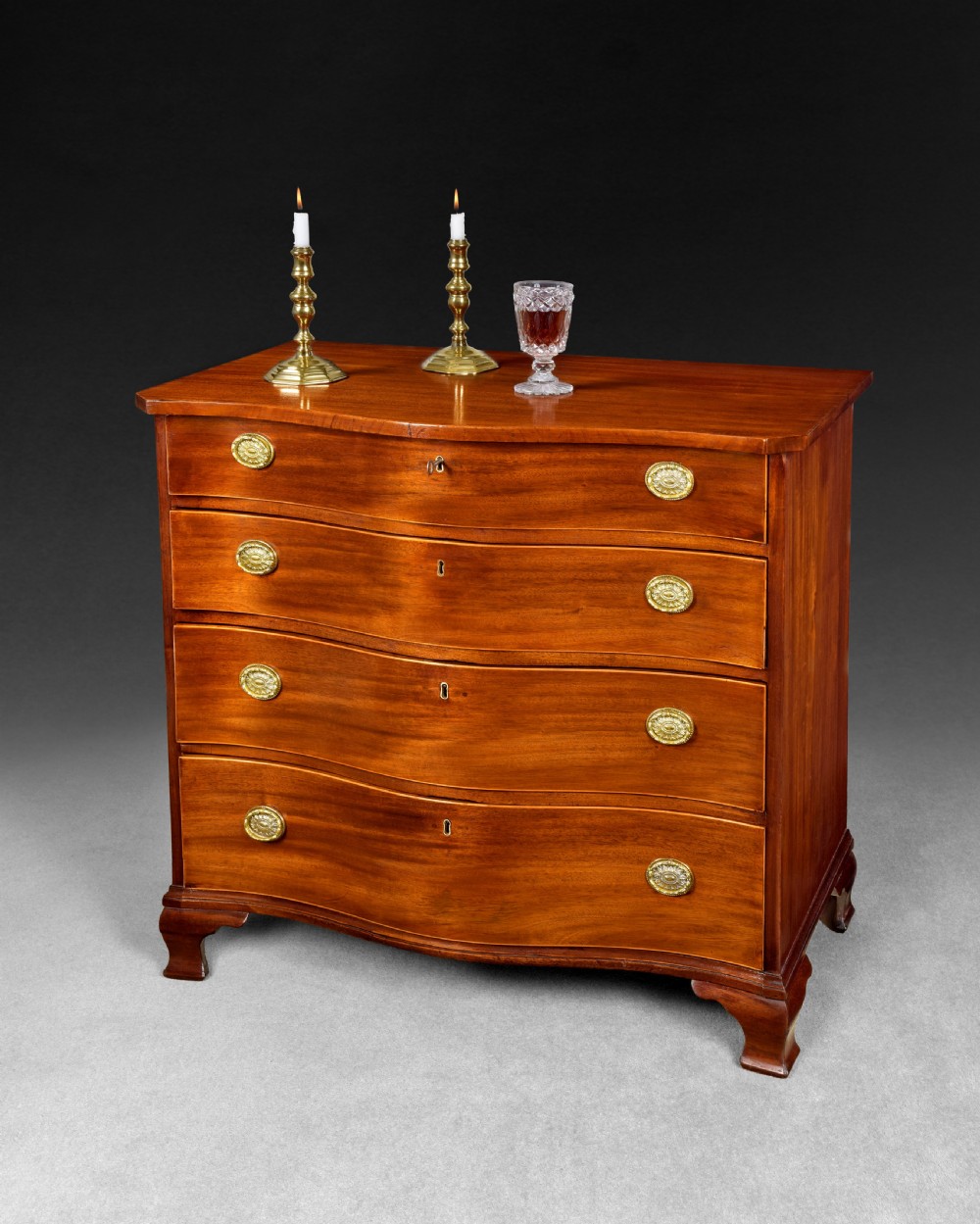 A George III mahogany chest of drawers featuring a serpentine front, four graduated drawers with brass oval handles, and bracket feet. View IX