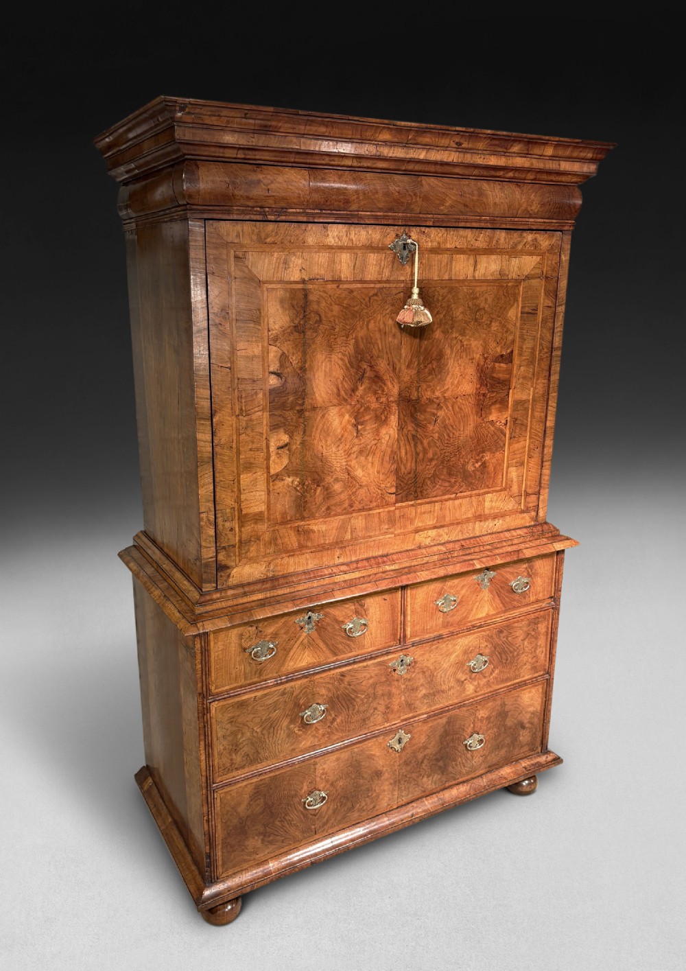 A William and Mary period walnut escritoire featuring a fall-front upper cabinet above a lower chest of drawers on bun feet.