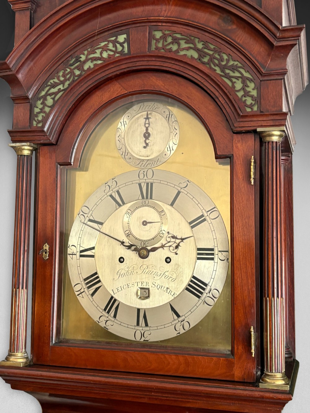 A Georgian longcase clock featuring a polished mahogany cabinet, brass dial with chapter ring, and decorative hood finials. View V