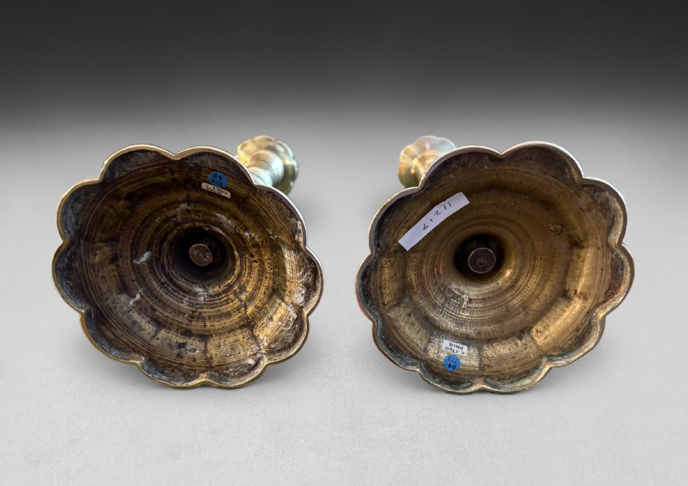 A pair of turned brass candlesticks with baluster shafts and scalloped petal-shaped bases. View II