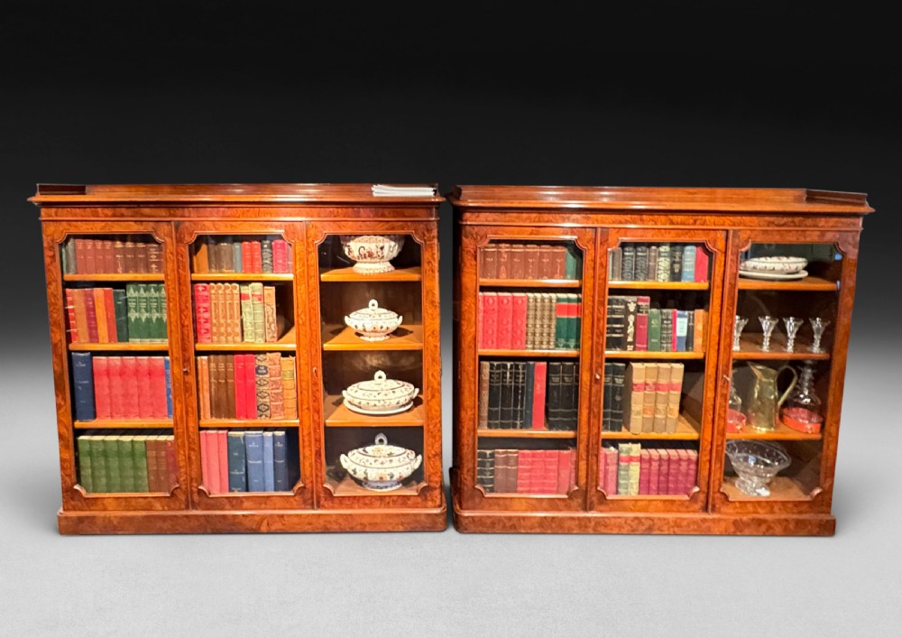 A pair of low Victorian walnut glazed bookcases featuring three arched glass doors and a plinth base.