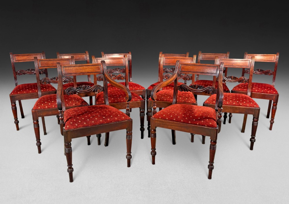 A set of twelve mahogany Regency dining chairs including ten side chairs and two carvers with reeded legs and red patterned upholstered seats.