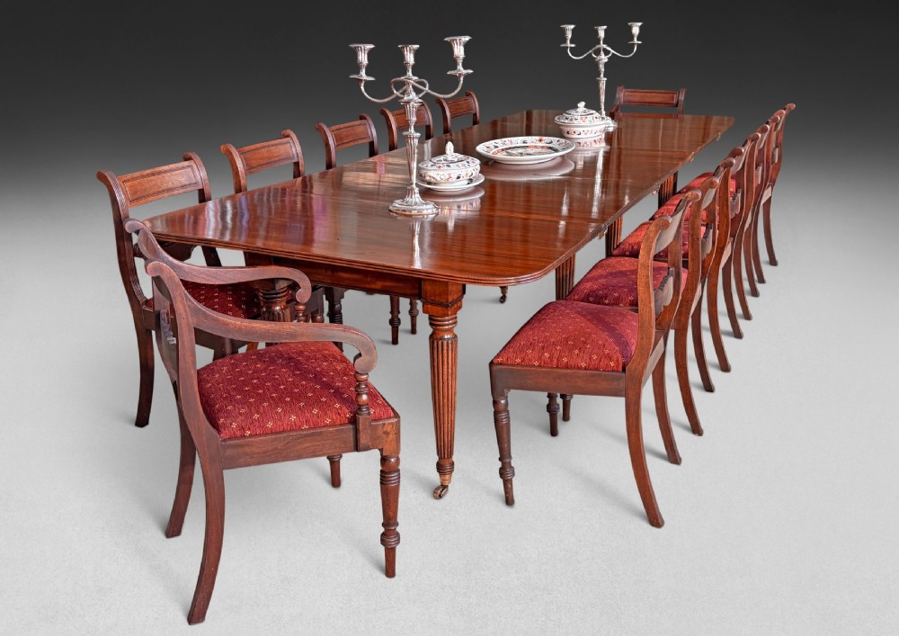 A set of twelve mahogany Regency dining chairs including ten side chairs and two carvers with reeded legs and red patterned upholstered seats. View II
