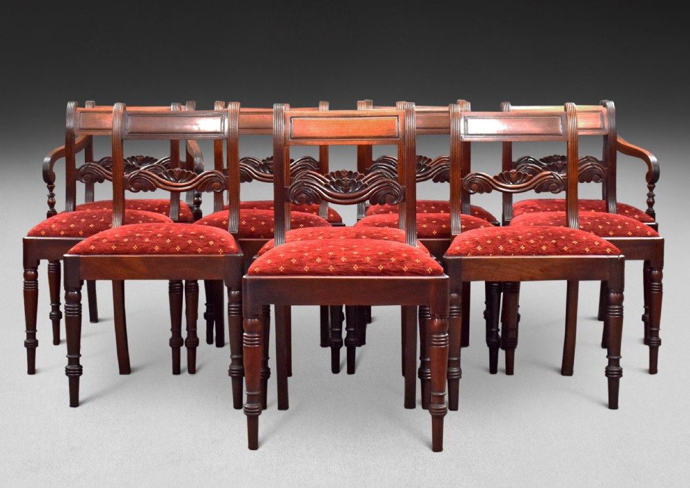 A set of twelve mahogany Regency dining chairs including ten side chairs and two carvers with reeded legs and red patterned upholstered seats. View VI