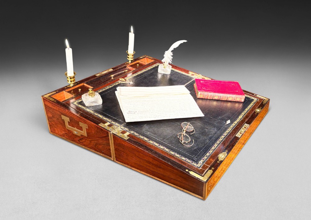 An opened Regency rosewood writing slope featuring brass inlay, brass candle sockets, side handles, and a dark leather writing surface.