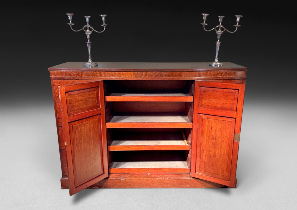 A Regency plum pudding mahogany low linen press featuring double central panelled doors flanked by eight drawers with brass handles on a plinth base. View II