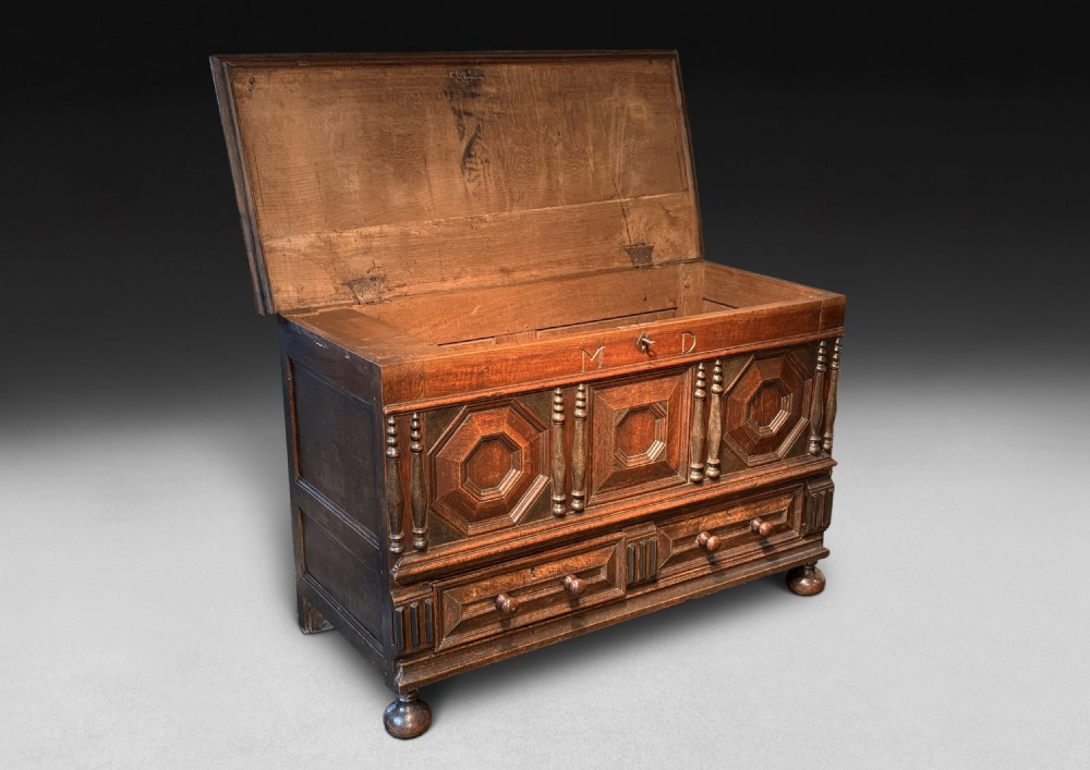 An 18th-century dark oak mule chest featuring geometric carved panels, split spindle turnings, two base drawers, and turned bun feet. View II