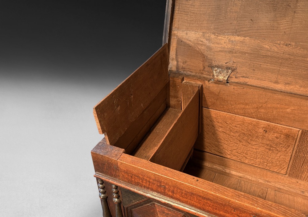 An 18th-century dark oak mule chest featuring geometric carved panels, split spindle turnings, two base drawers, and turned bun feet. View III