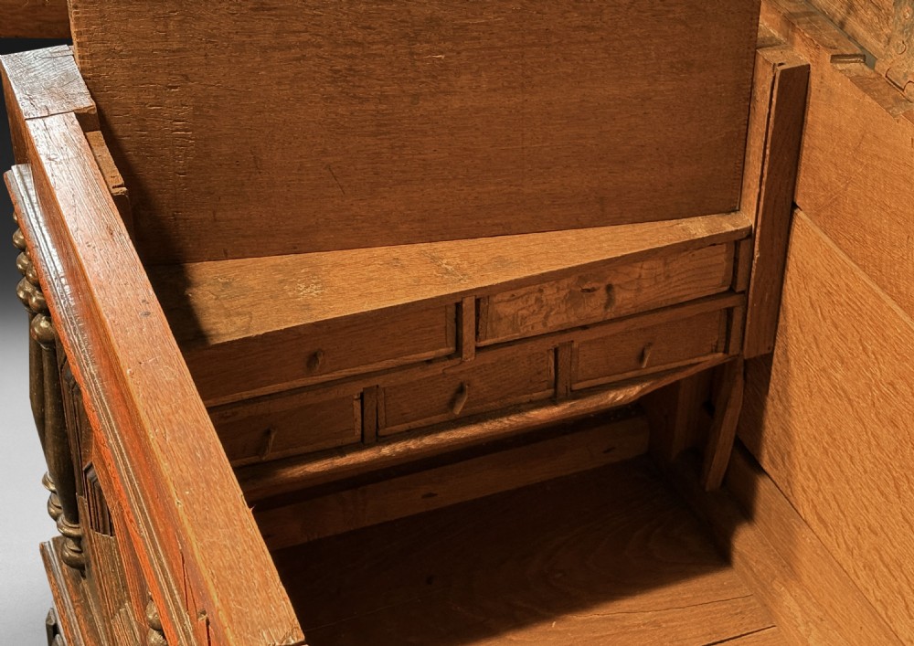 An 18th-century dark oak mule chest featuring geometric carved panels, split spindle turnings, two base drawers, and turned bun feet. View IV