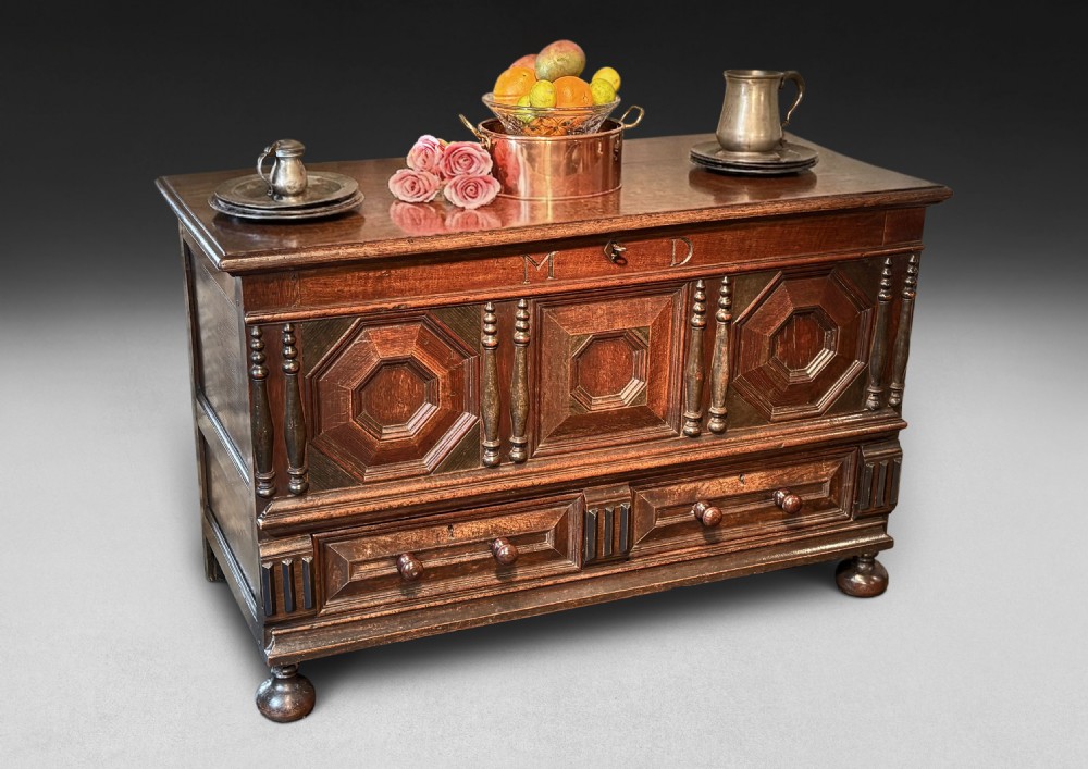 An 18th-century dark oak mule chest featuring geometric carved panels, split spindle turnings, two base drawers, and turned bun feet. View V