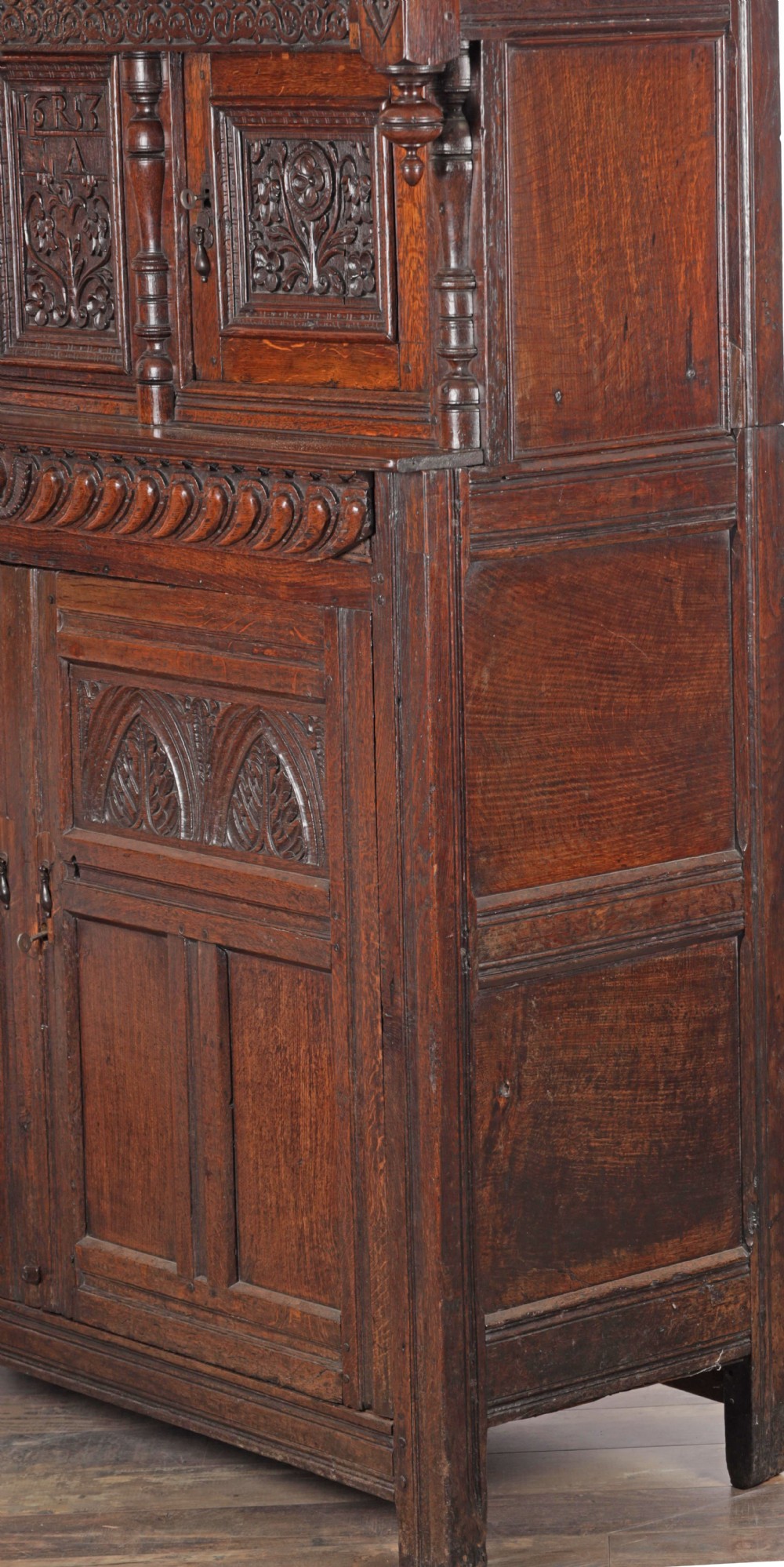 A mid-17th century carved dark oak press cupboard featuring relief-carved upper panels, turned balusters, arcaded lower doors, and an inscribed date of 1653. View III