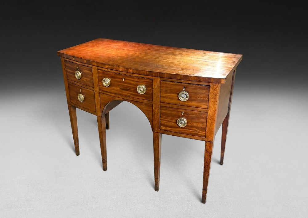 A George III mahogany bowfront sideboard featuring five drawers with circular brass ring handles, an arched central apron, and four square tapered legs.