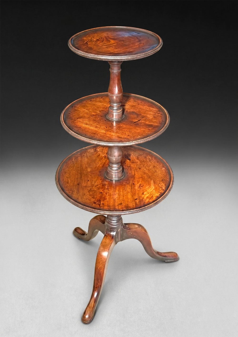 A George III mahogany three-tier dumb waiter featuring graduated circular trays on a turned central column supported by a tripod base.