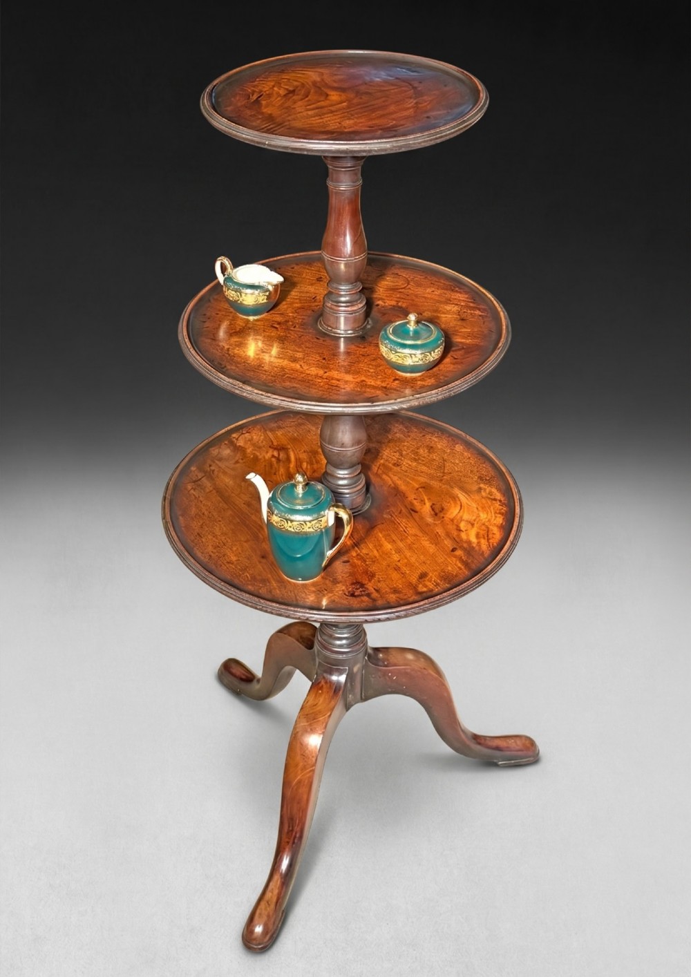 A George III mahogany three-tier dumb waiter featuring graduated circular trays on a turned central column supported by a tripod base. View II