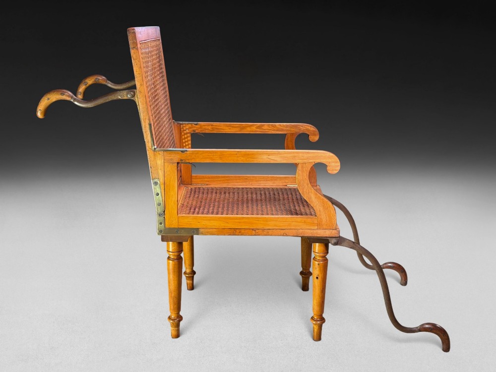 A mid-19th-century wooden campaign armchair with a woven cane back and seat, brass corner mounts, turned legs, and extendable curved handles.