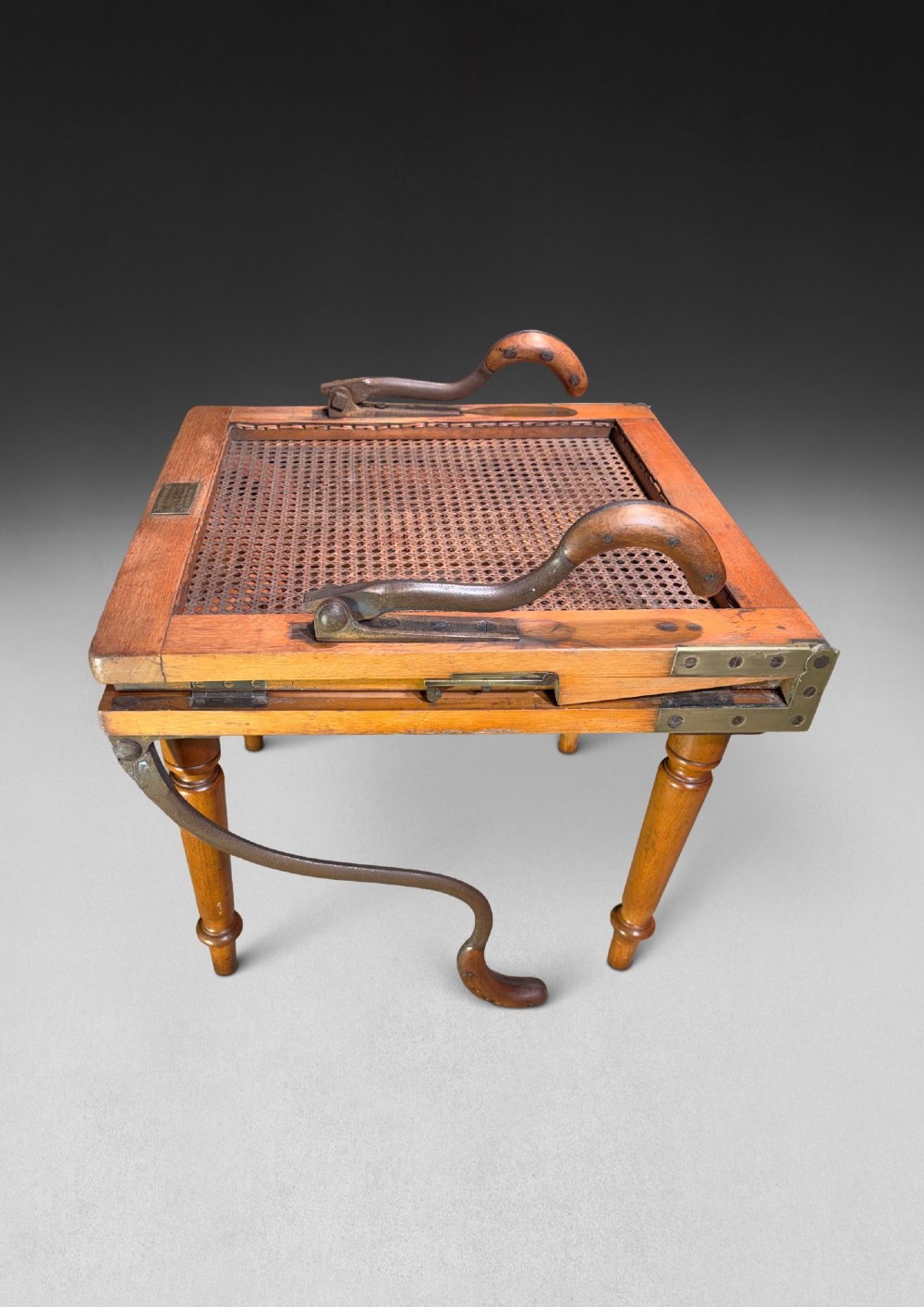 A mid-19th-century wooden campaign armchair with a woven cane back and seat, brass corner mounts, turned legs, and extendable curved handles. View III