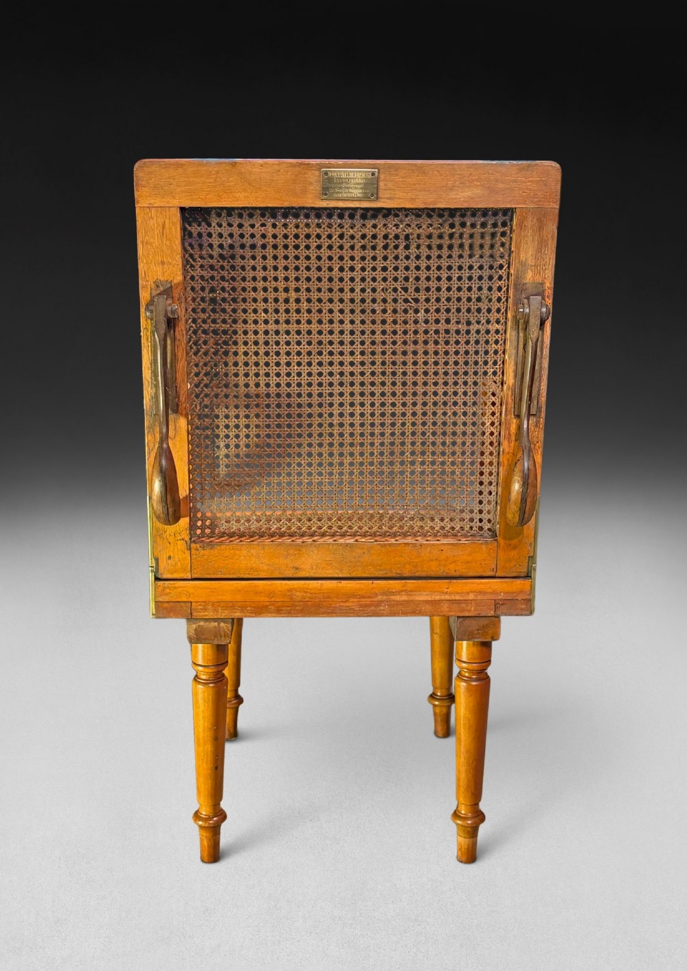 A mid-19th-century wooden campaign armchair with a woven cane back and seat, brass corner mounts, turned legs, and extendable curved handles. View VII