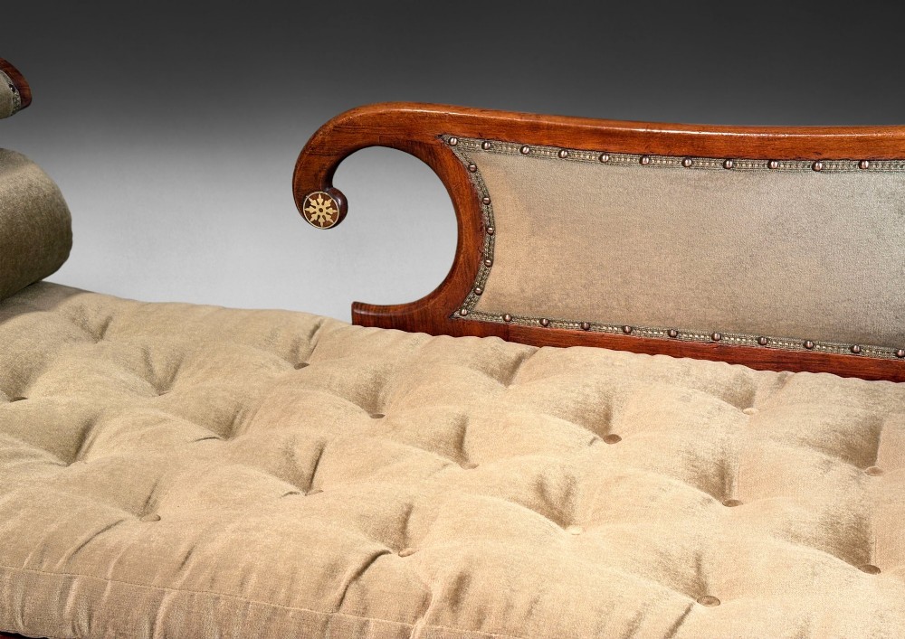 Regency simulated rosewood chaise longue with brass inlay, featuring asymmetrical scroll ends, turned brass-castor legs, olive green button-tufted upholstery, and matching bolster cushions. View III