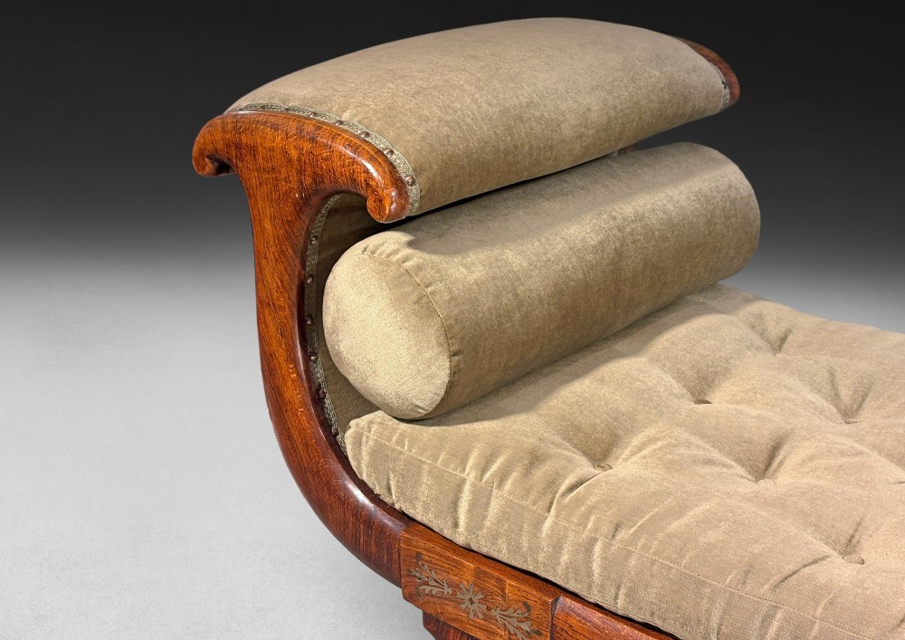 Regency simulated rosewood chaise longue with brass inlay, featuring asymmetrical scroll ends, turned brass-castor legs, olive green button-tufted upholstery, and matching bolster cushions. View IV