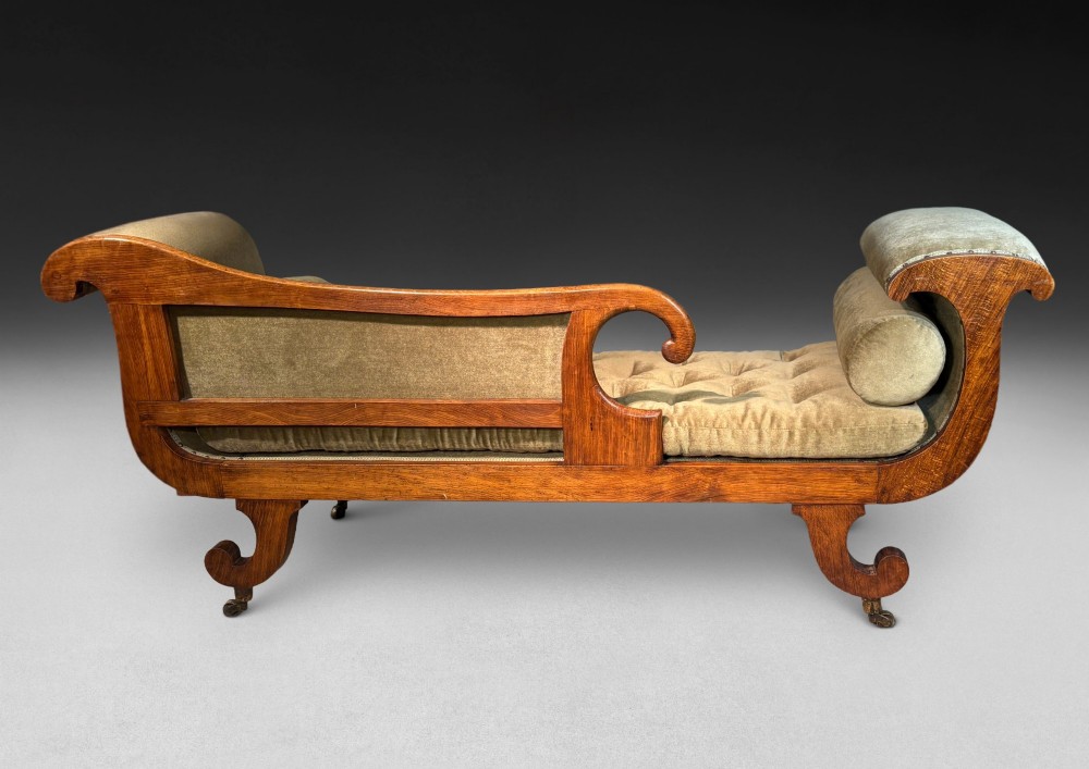 Regency simulated rosewood chaise longue with brass inlay, featuring asymmetrical scroll ends, turned brass-castor legs, olive green button-tufted upholstery, and matching bolster cushions. View VI