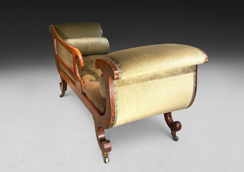 Regency simulated rosewood chaise longue with brass inlay, featuring asymmetrical scroll ends, turned brass-castor legs, olive green button-tufted upholstery, and matching bolster cushions. View VII