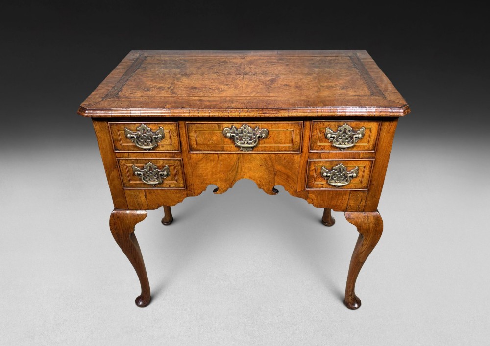 A George II period burr walnut lowboy featuring cabriole legs ending in pad feet, multiple drawers with brass drop handles, and a shaped apron.