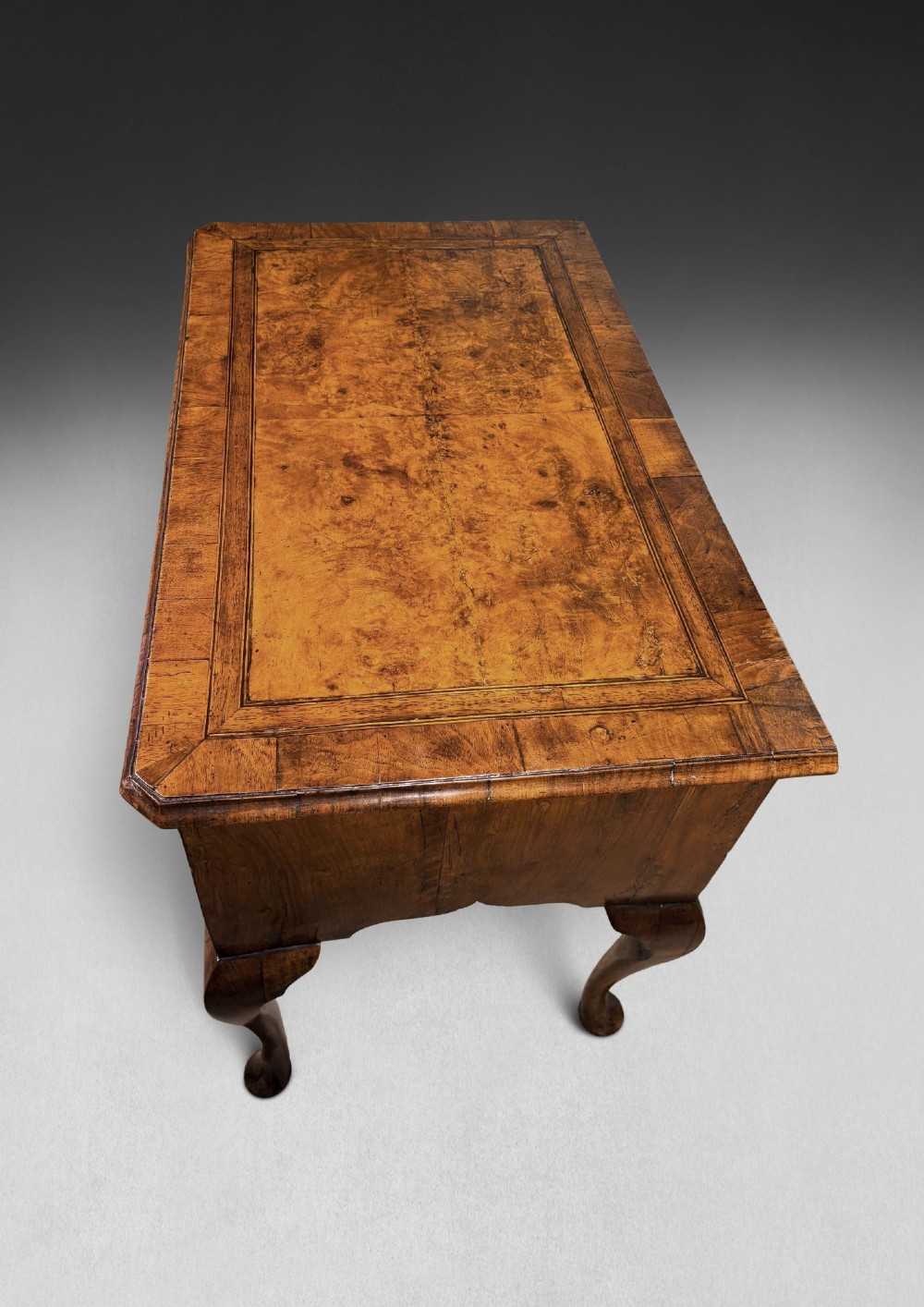 A George II period burr walnut lowboy featuring cabriole legs ending in pad feet, multiple drawers with brass drop handles, and a shaped apron. View IV