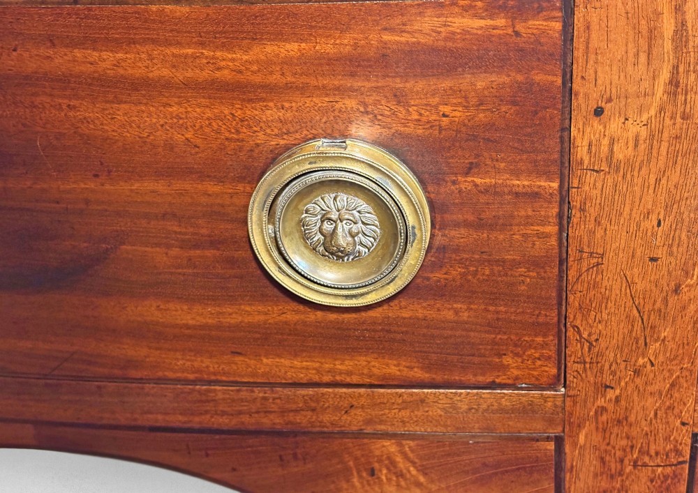 A George III bow-fronted mahogany sideboard featuring multiple drawers with brass ring handles, a central arch, and tapered square legs. View II