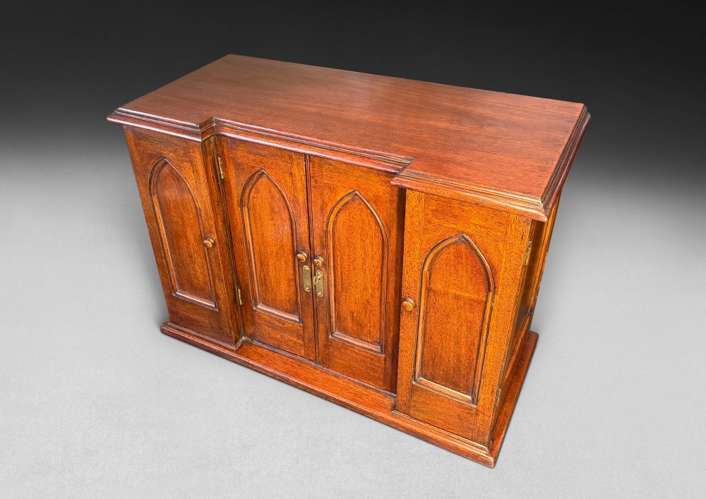 A nineteenth-century oak tabletop collectors cabinet featuring breakfront doors with carved Gothic arch panels and turned wooden knobs.