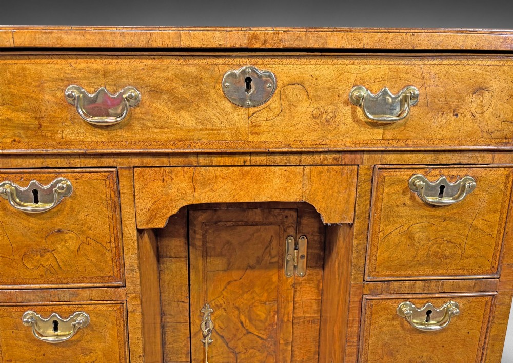 A George I period kneehole desk made from figured walnut with brass drop handles, bracket feet, and a central recessed cupboard. View II
