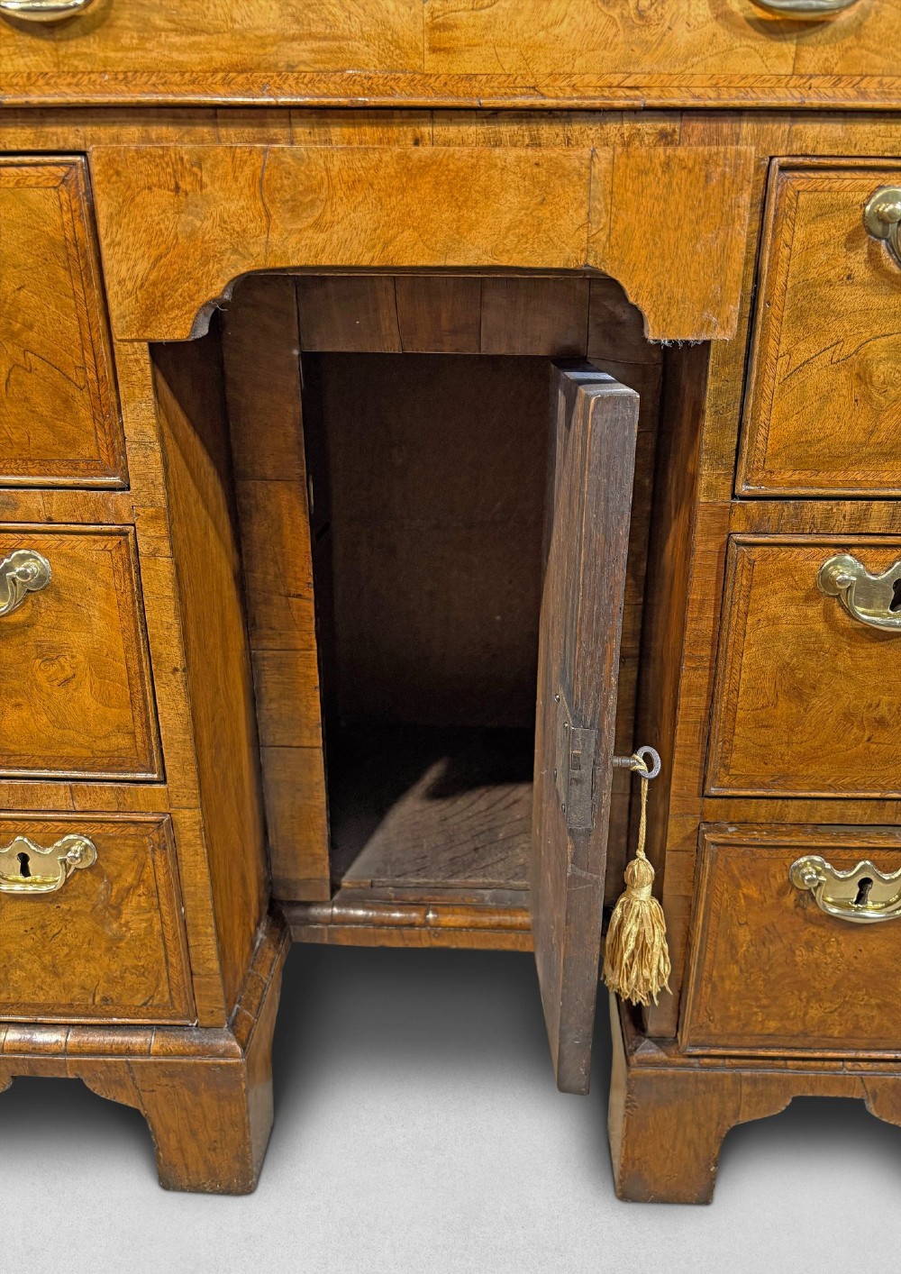 A George I period kneehole desk made from figured walnut with brass drop handles, bracket feet, and a central recessed cupboard. View III