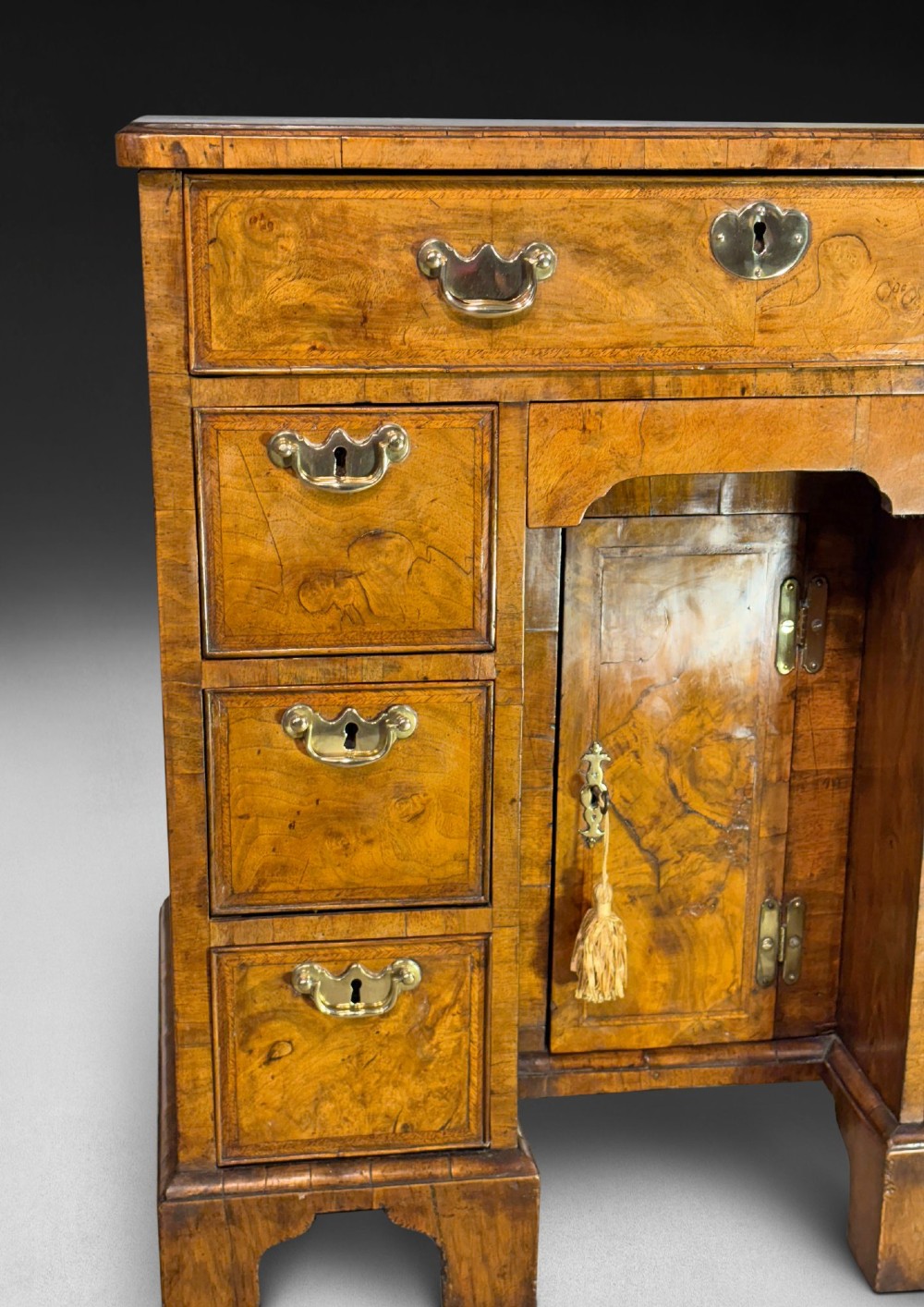 A George I period kneehole desk made from figured walnut with brass drop handles, bracket feet, and a central recessed cupboard. View VI