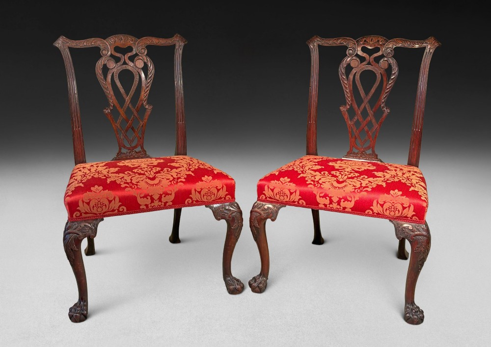 A pair of carved mahogany Chippendale style side chairs with pierced splats, cabriole legs, and red patterned damask upholstered seats.