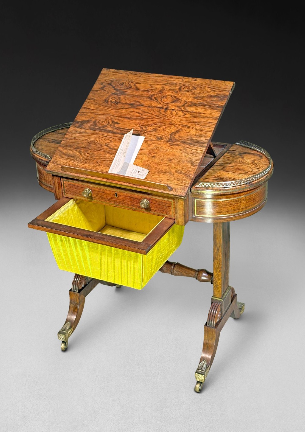A Regency rosewood compendium table with brass stringing inlay, a single drawer, a pleated yellow silk basket underneath, and splayed legs ending in brass castors. View V