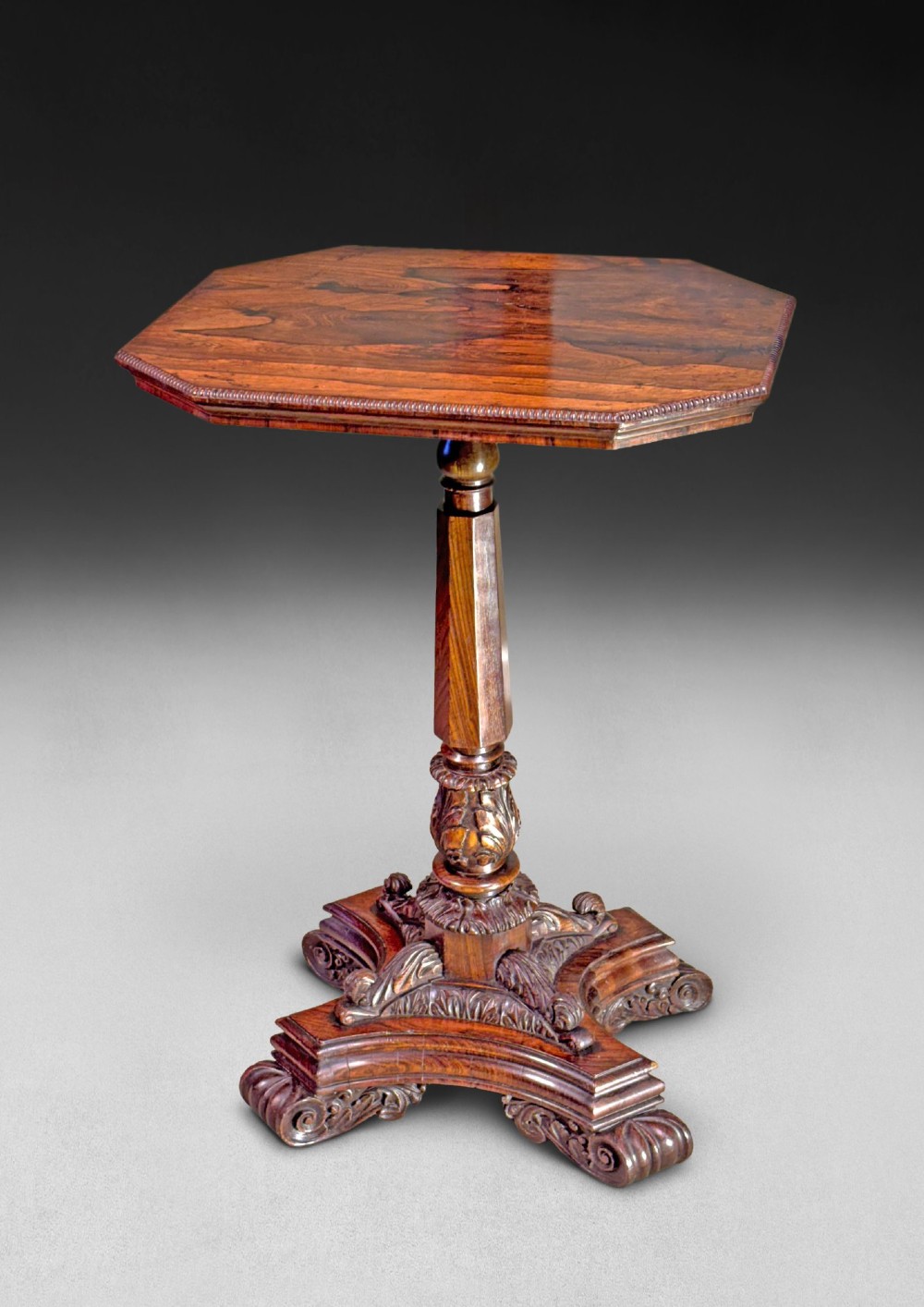 An antique Regency rosewood octagonal wine table with a faceted central column and a carved quadform base.