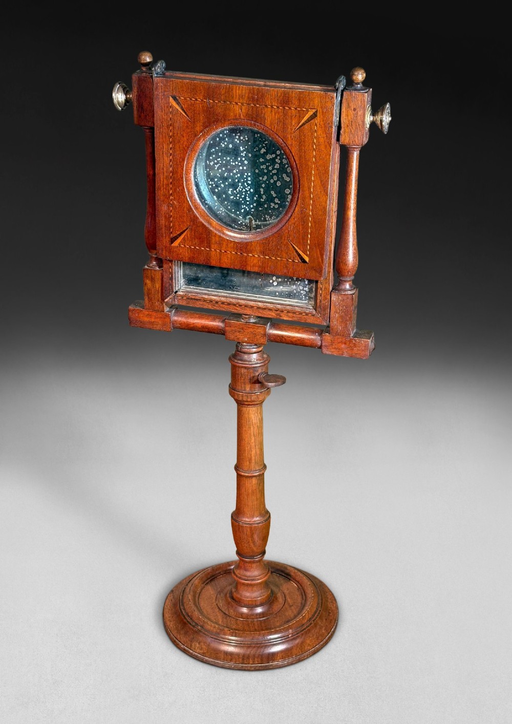 A Regency mahogany optical zograscope on a turned pedestal stand featuring an inlaid rectangular frame containing a circular convex magnifying lens above an adjustable mirror.