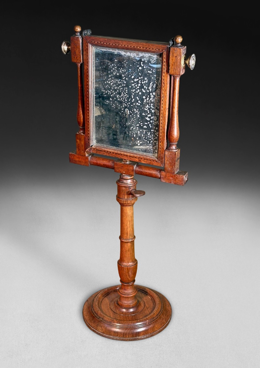 A Regency mahogany optical zograscope on a turned pedestal stand featuring an inlaid rectangular frame containing a circular convex magnifying lens above an adjustable mirror. View II