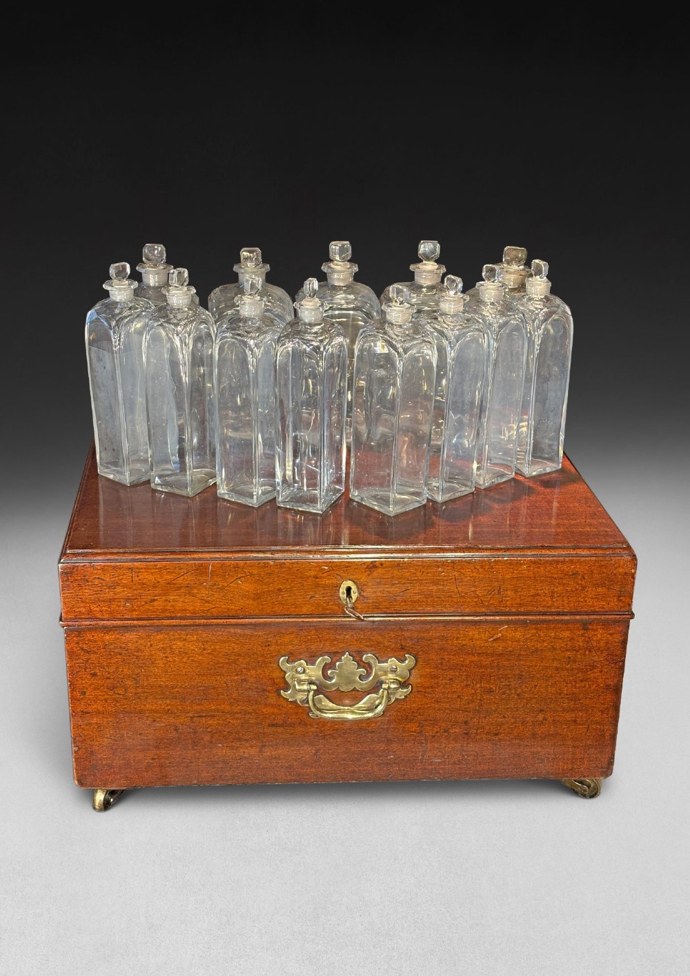 An open George III mahogany decanter chest displaying fitted glass decanters, internal compartments, velvet lid lining, and brass hardware. View III