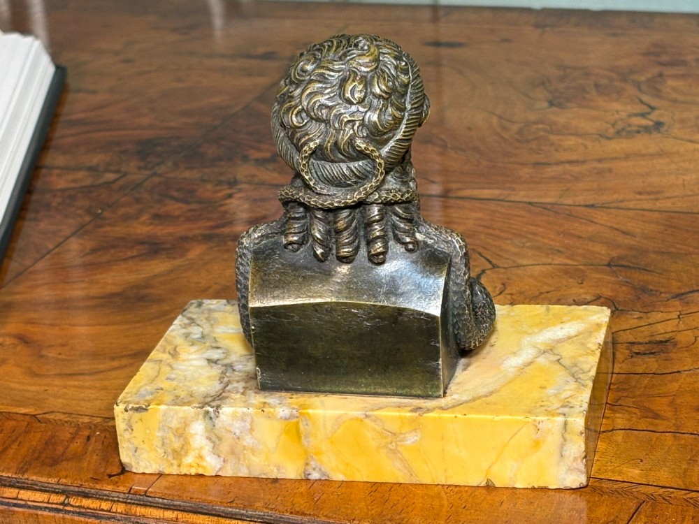 A patinated dark bronze bust of a bearded deity featuring a coiled serpent, mounted on a rectangular yellow marble base. View II