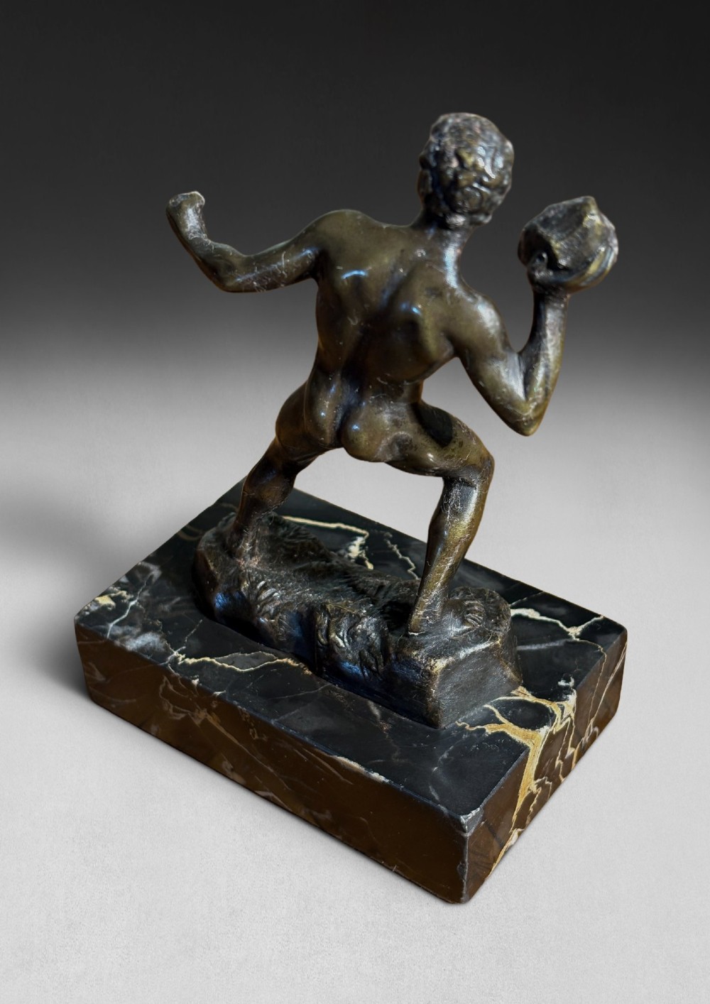 A patinated dark bronze figurine depicting a nude ancient Greek male athlete holding a stone, mounted on a rectangular black marble base with white veining. View III