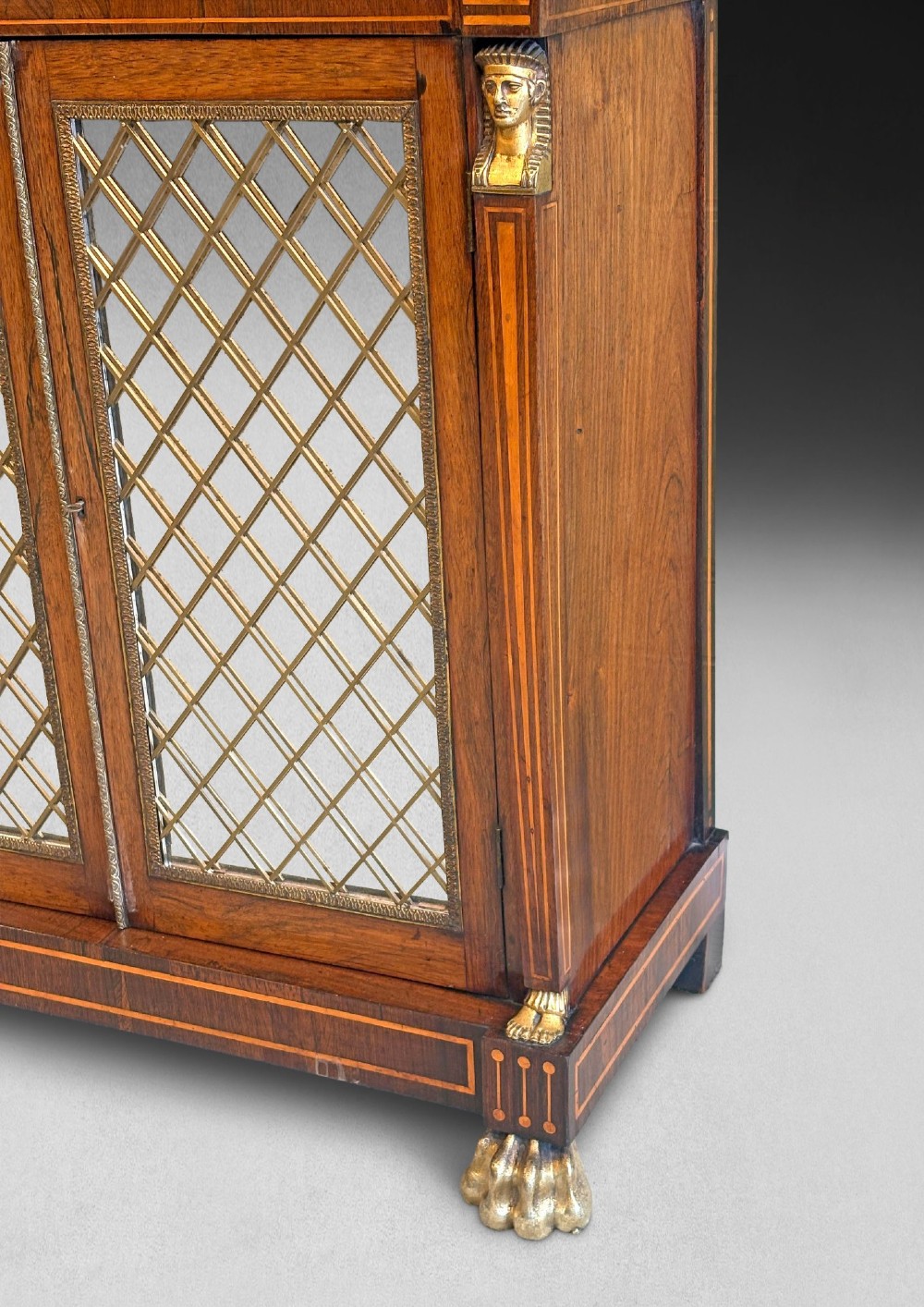 A pair of Regency rosewood chiffoniers featuring boxwood stringing, brass lattice panel doors, upper display shelves with brass galleries, and claw feet. View IV
