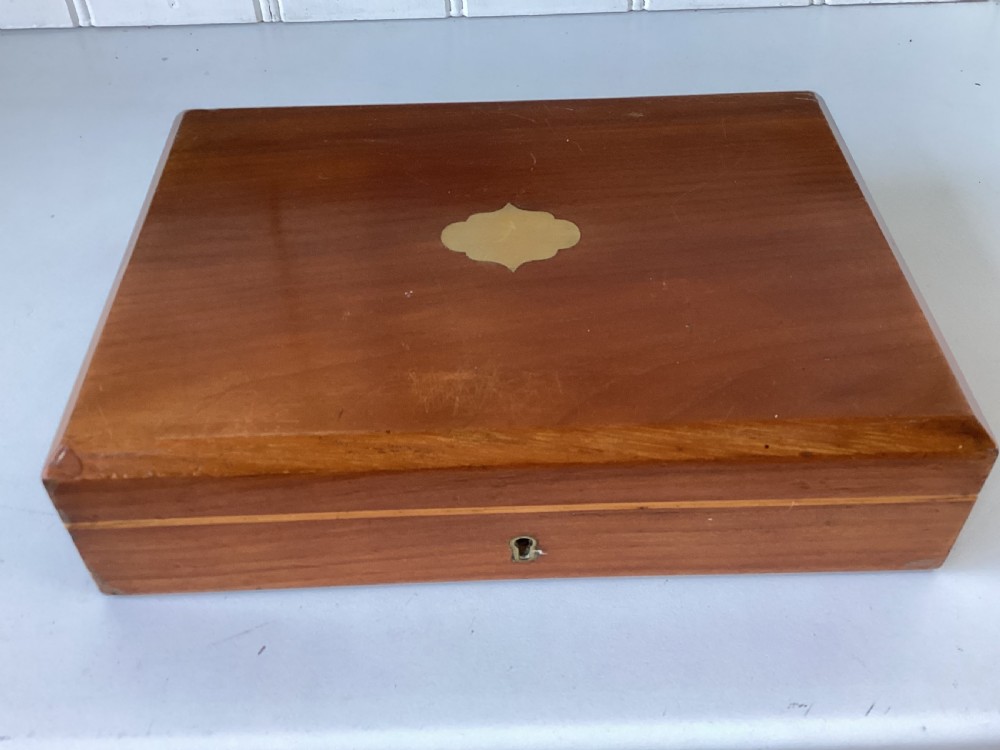 A rectangular mahogany jewellery box with a fitted lid, featuring an inlaid brass shield on top and a central brass keyhole on the front casing.