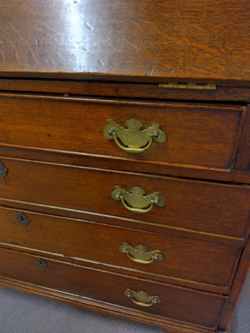 fig 2. An 18th-century oak bureau bookcase featuring a twin-panelled upper cabinet above a fall-front desk and four graduated long drawers with brass handles.