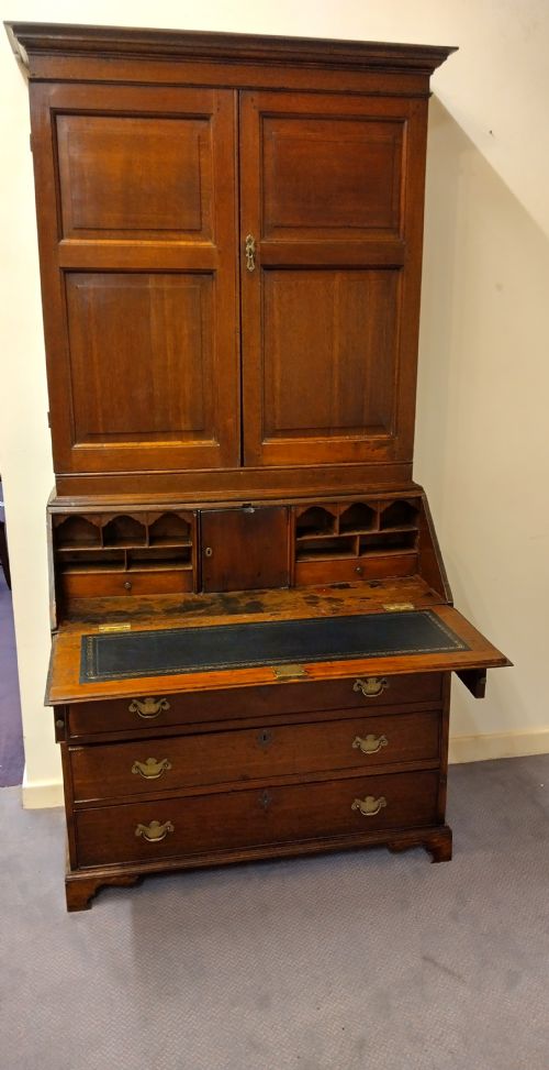 fig 1. An 18th-century oak bureau bookcase featuring a twin-panelled upper cabinet above a fall-front desk and four graduated long drawers with brass handles.