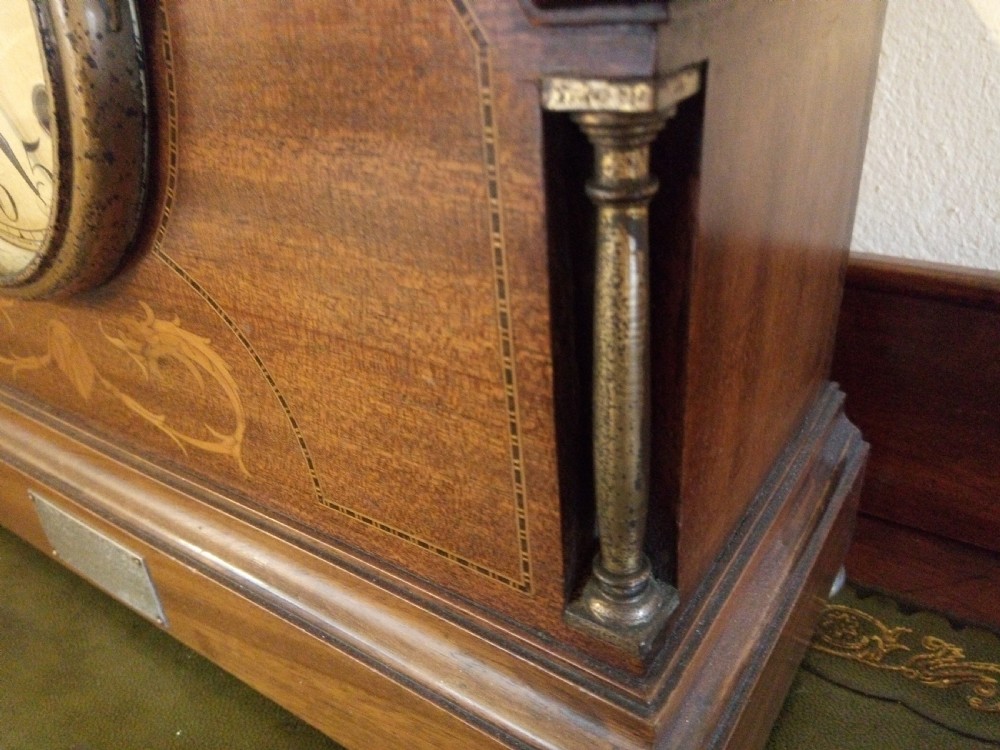 An Edwardian dome top mahogany mantel clock featuring floral marquetry inlay, brass side columns, and an Arabic numeral dial. View II