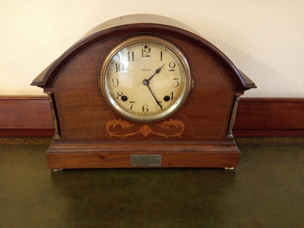 An Edwardian dome top mahogany mantel clock featuring floral marquetry inlay, brass side columns, and an Arabic numeral dial. View IV