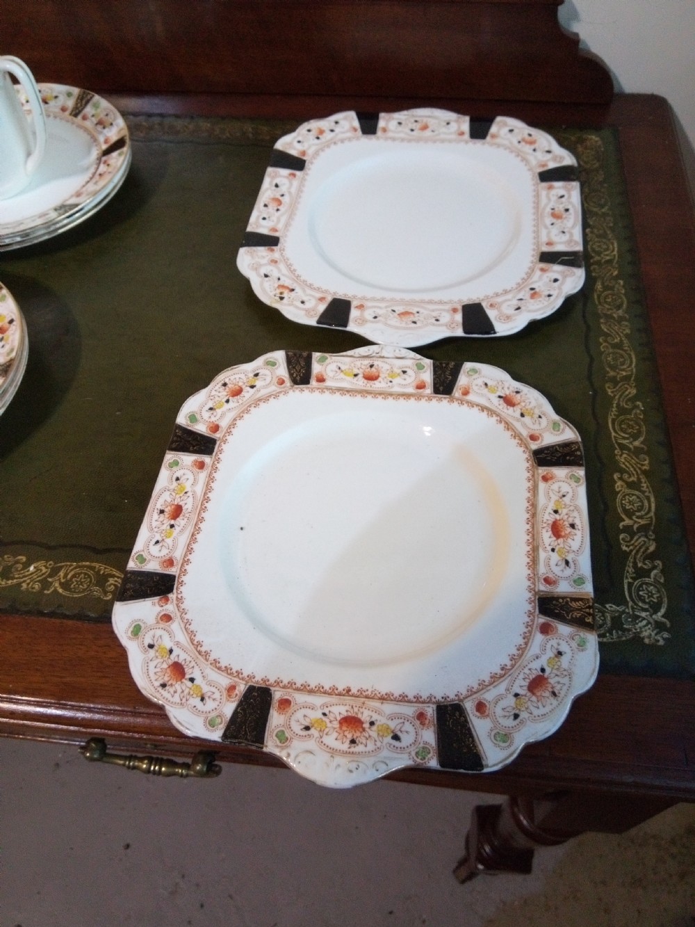 A twenty-one piece Gladstone bone china tea service arranged on a surface, displaying white teacups, saucers, side plates, a milk pitcher, a slop bowl, and a square serving plate decorated with black geometric borders and gilded rims. View IV